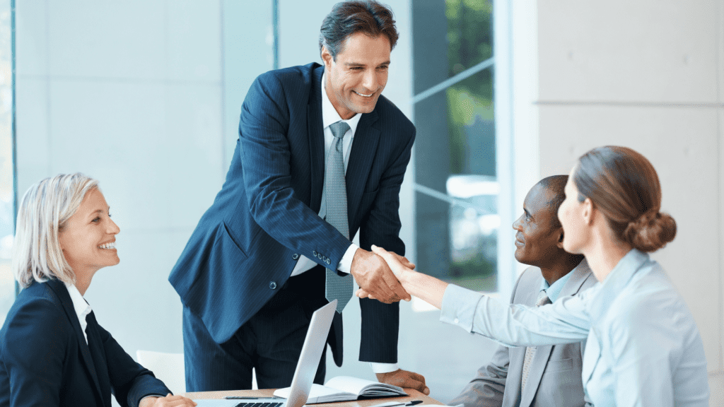 man in suit shaking female hand with smile on his face and two other colleagues present