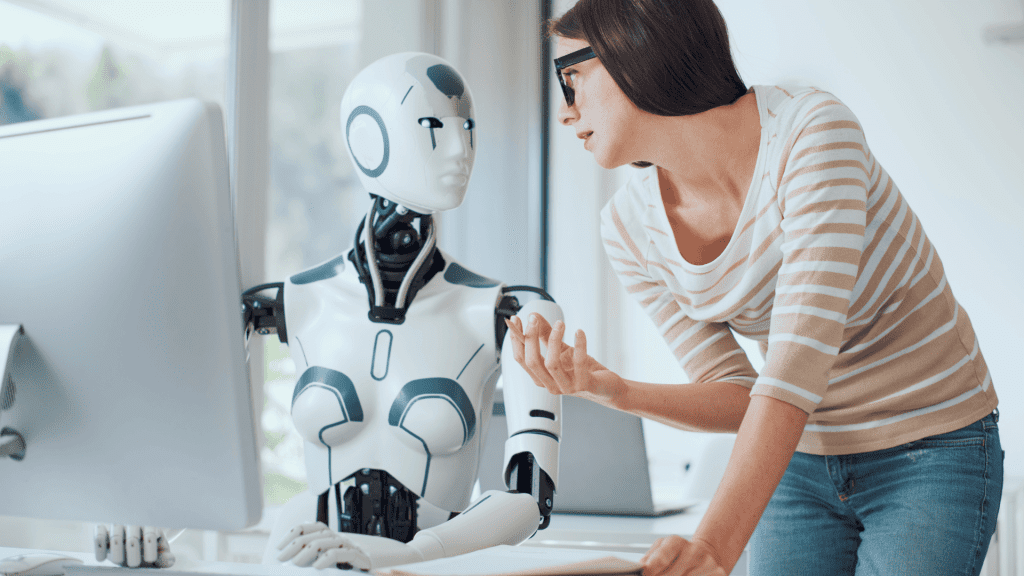 female worker talking to a robot while standing in front of a computer